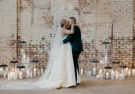 Wedding couple kissing with an industrial brick background and surrounded by candles